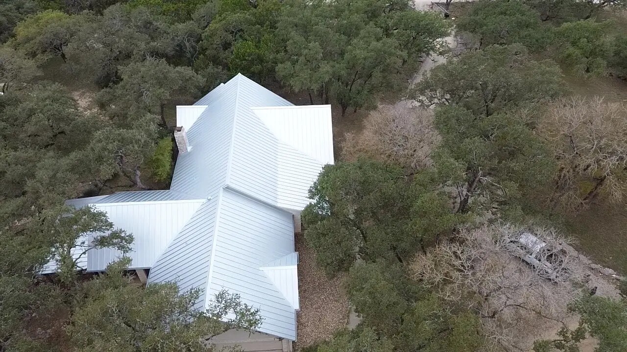 Aerial view of a house with a light metal roof among trees
